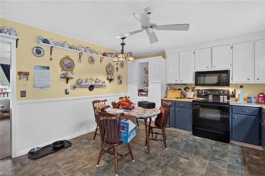 Kitchen with blue lower cabinets, black appliances, and a round dining table beneath a ceiling fan.
