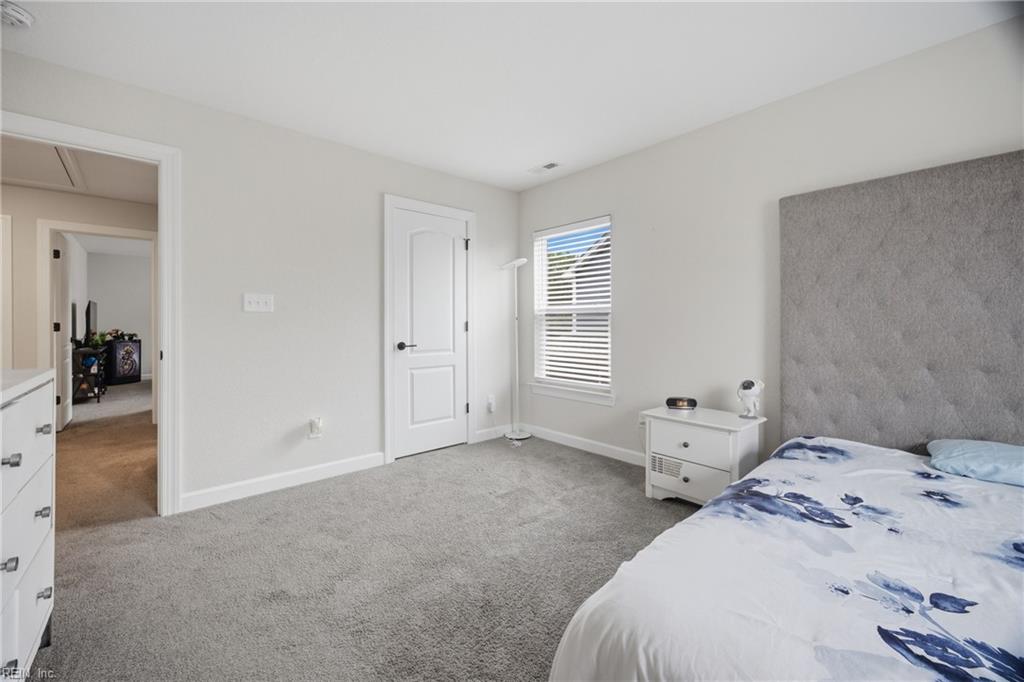 Bedroom with a tall tufted gray headboard, floral bedding, and carpeted floor.