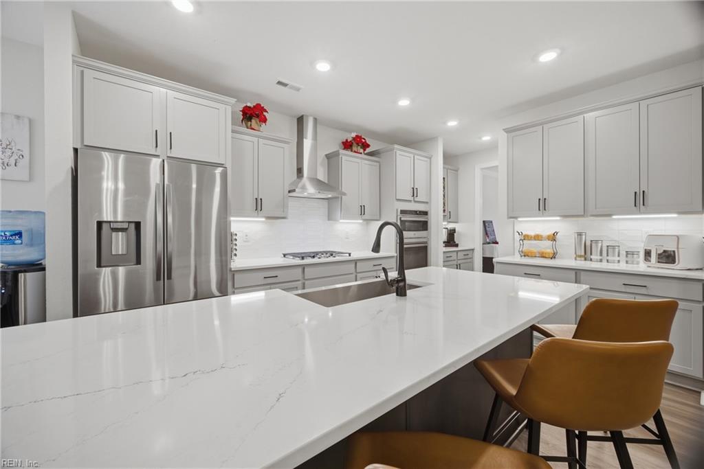 Kitchen with a large white island, stainless steel appliances, and brown bar stools.