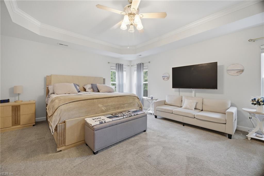 Bedroom with a king-size bed, tray ceiling, and a sitting area with a white sofa and television.