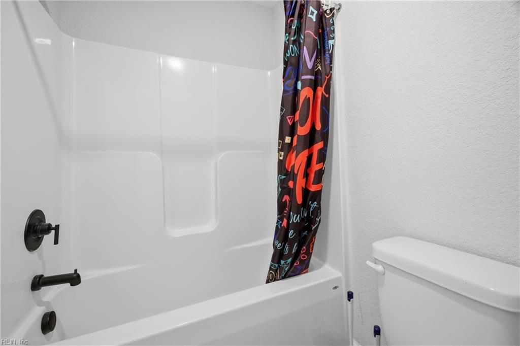Bathroom with a white tub and shower, colorful curtain, and black fixtures.