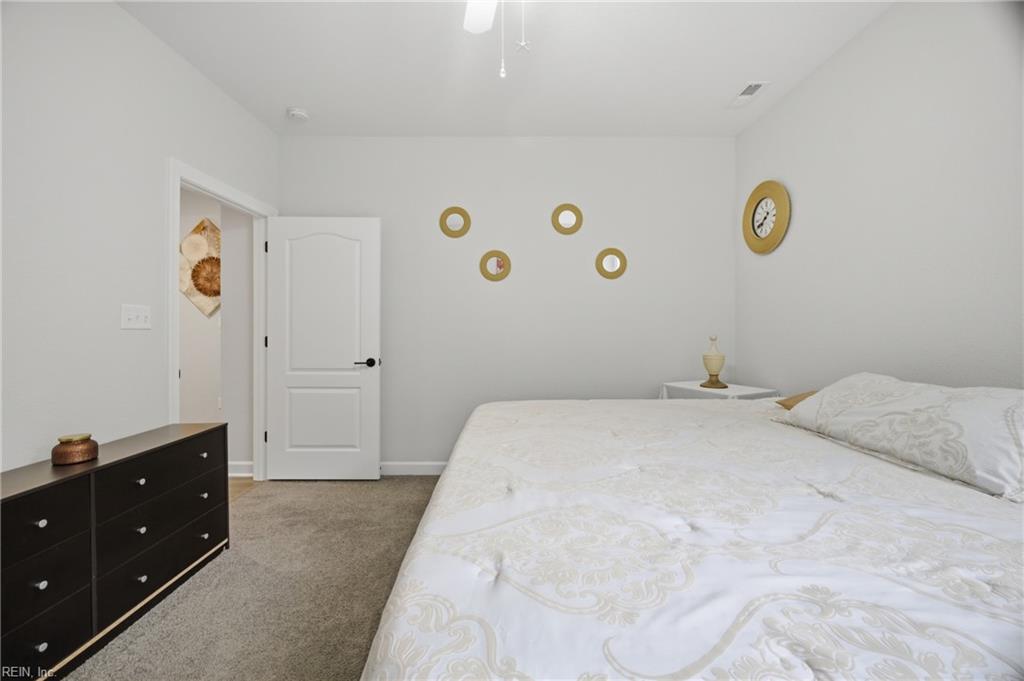 Bedroom with white patterned bedding, a dark dresser, and beige carpet.