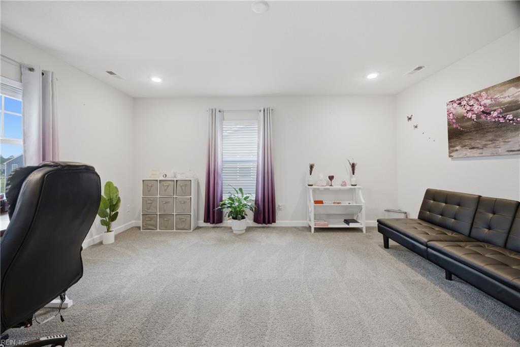 Carpeted living room with black seating, purple curtains, and a white display shelf.