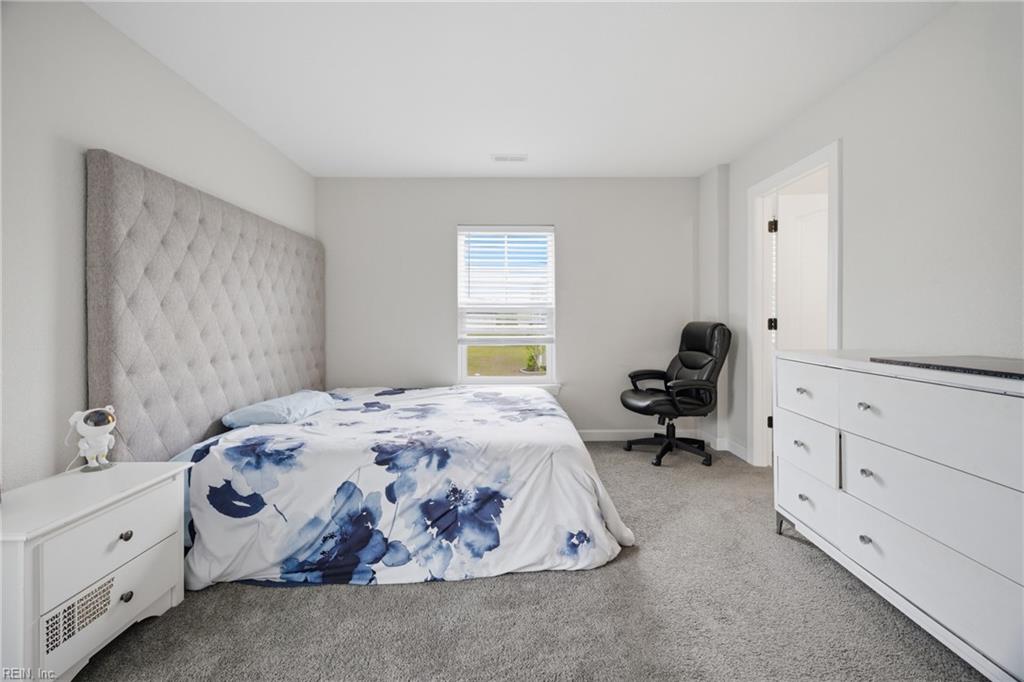 Bedroom with a tall tufted headboard, blue floral bedding, white dresser, and carpeted floor.
