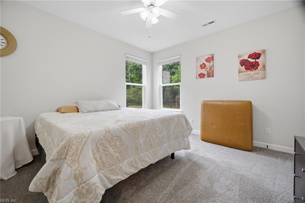 Bedroom with a patterned bedspread, two windows overlooking greenery, and a tan upholstered chair.