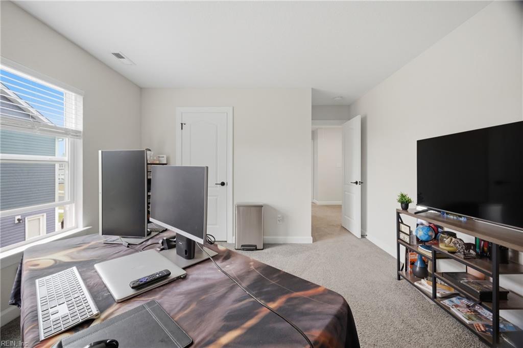 Bedroom office with two computer monitors on a bed and a TV on a media stand.