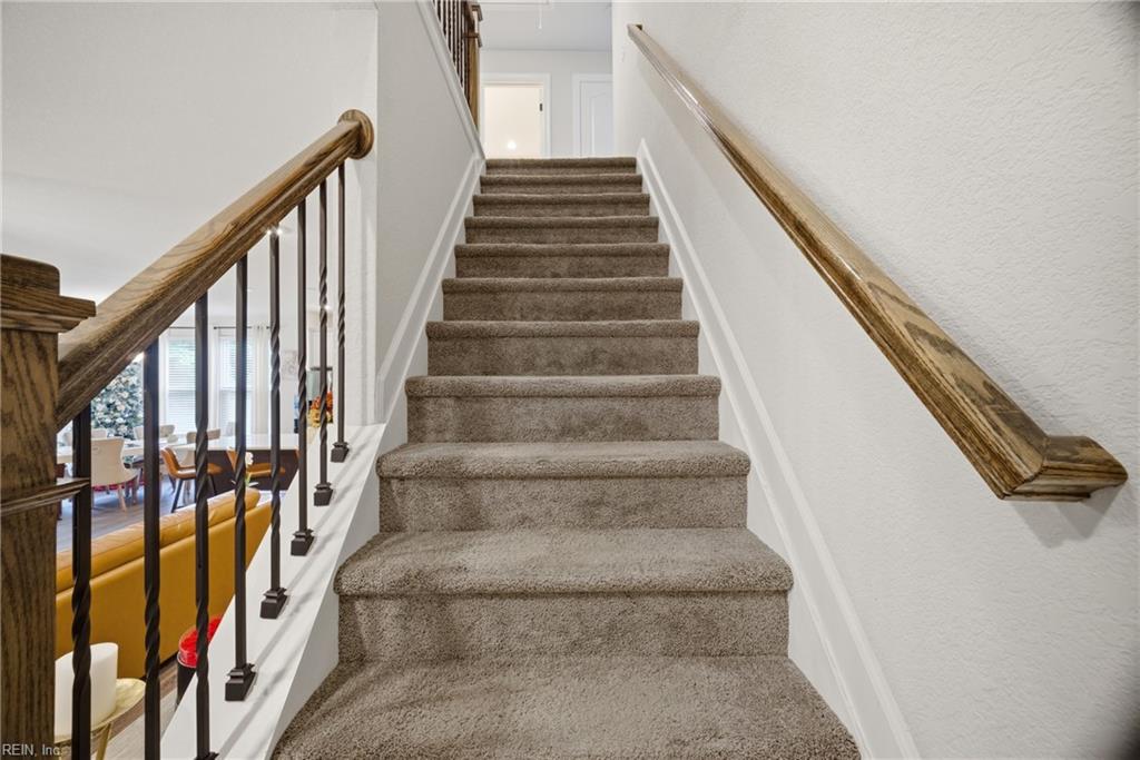 Carpeted staircase with wooden handrails and dark metal balusters overlooking a furnished living area.