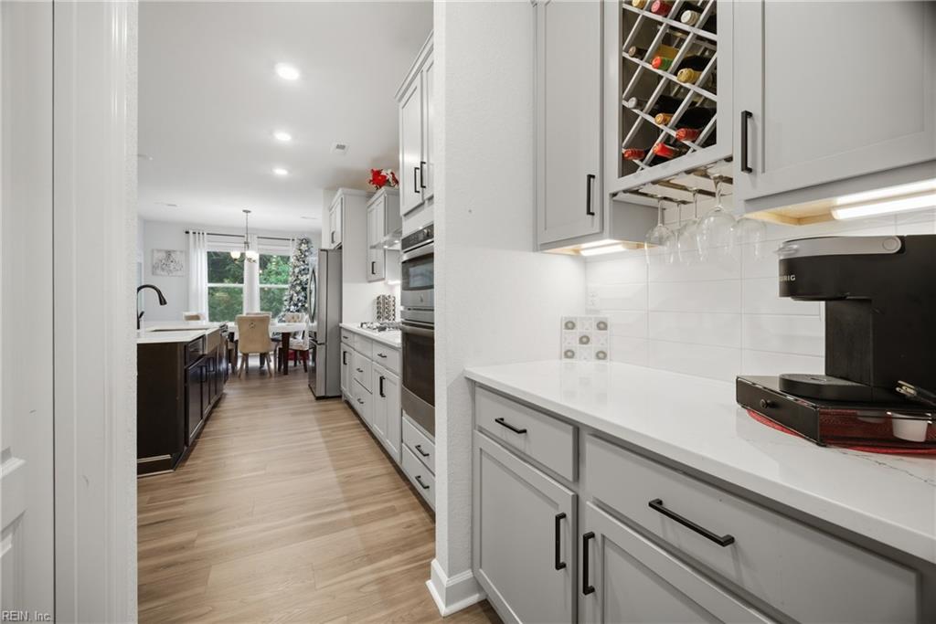 Bright kitchen with white cabinets, a built-in wine rack, and a dark island leading to a dining area.