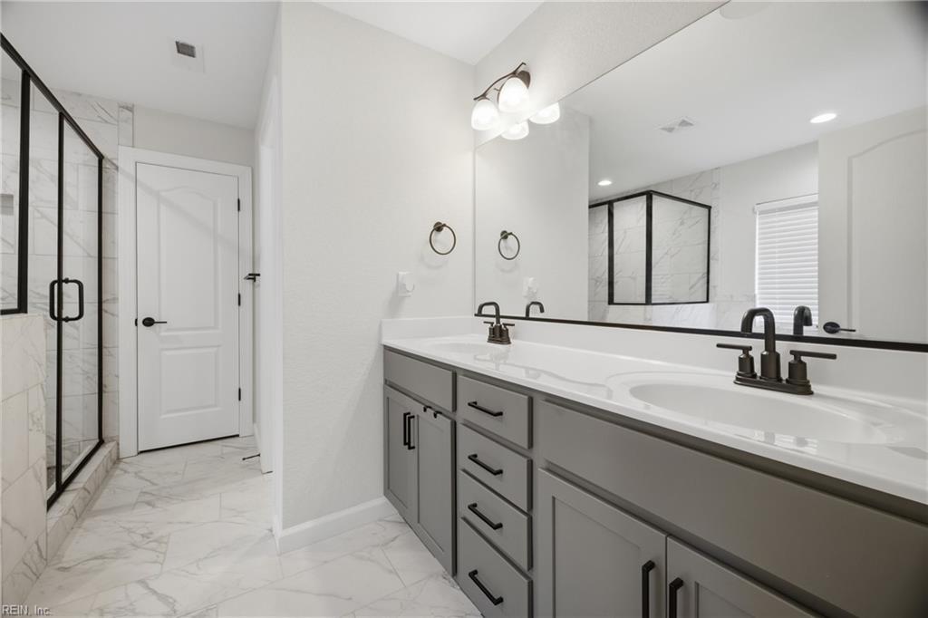 Bathroom with a long gray double vanity, marble-look tile, and a black-framed glass shower.
