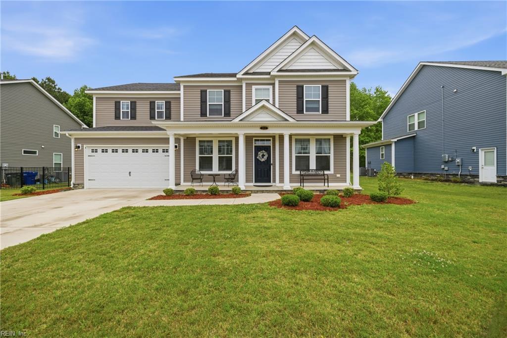 Two-story taupe house with a covered porch, attached garage, and broad green lawn.