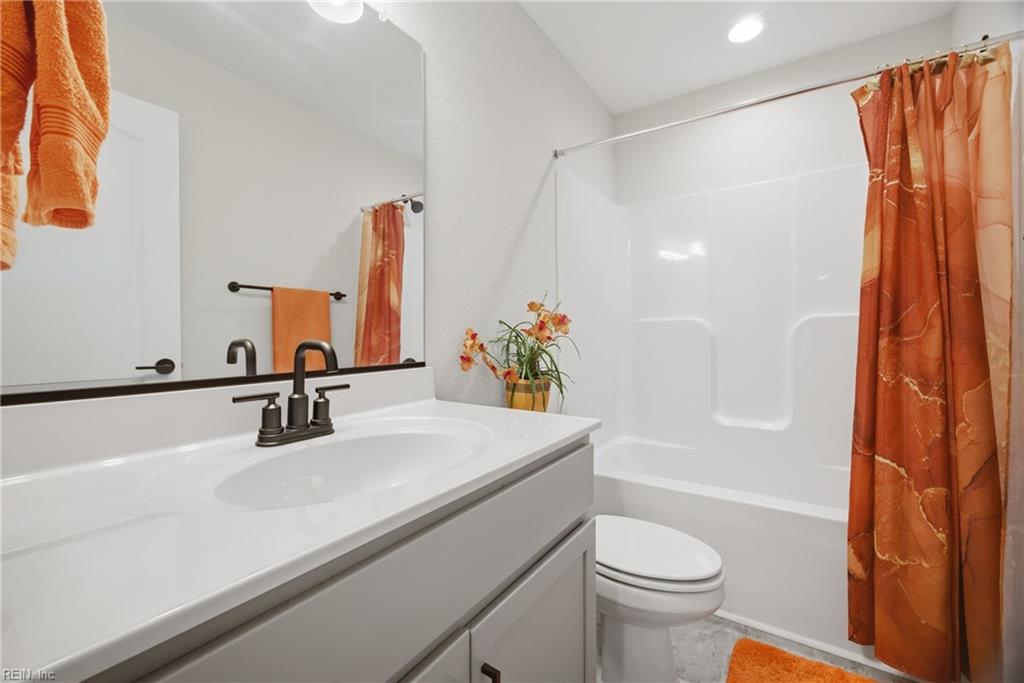 Bathroom with a white vanity and tub-shower, accented by orange towels and curtains.