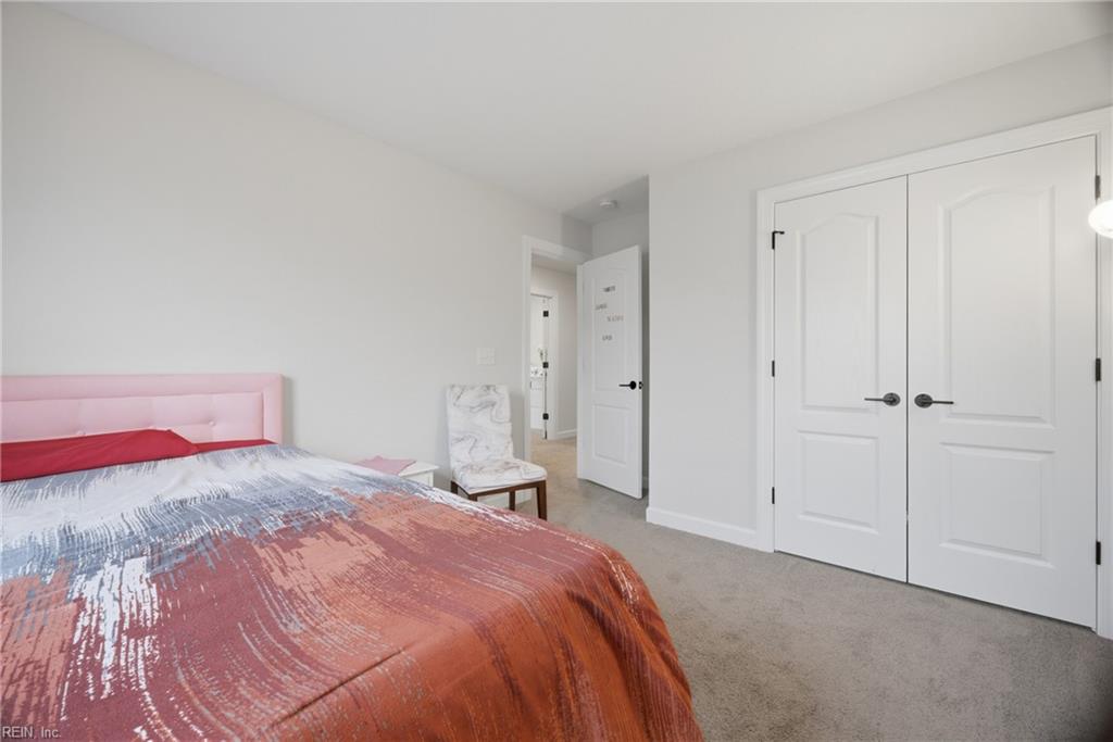 Bedroom with a pink upholstered headboard, patterned bedding, white closet doors, and a marble-patterned chair.