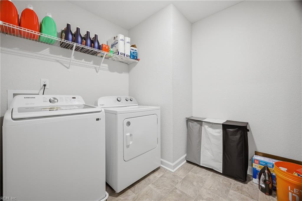 Laundry room with white washer and dryer, overhead wire shelf, and three-compartment hamper.