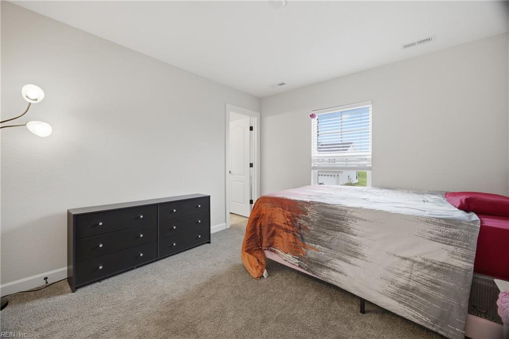 Bedroom with a patterned bedspread, pink pillows, and a black dresser.