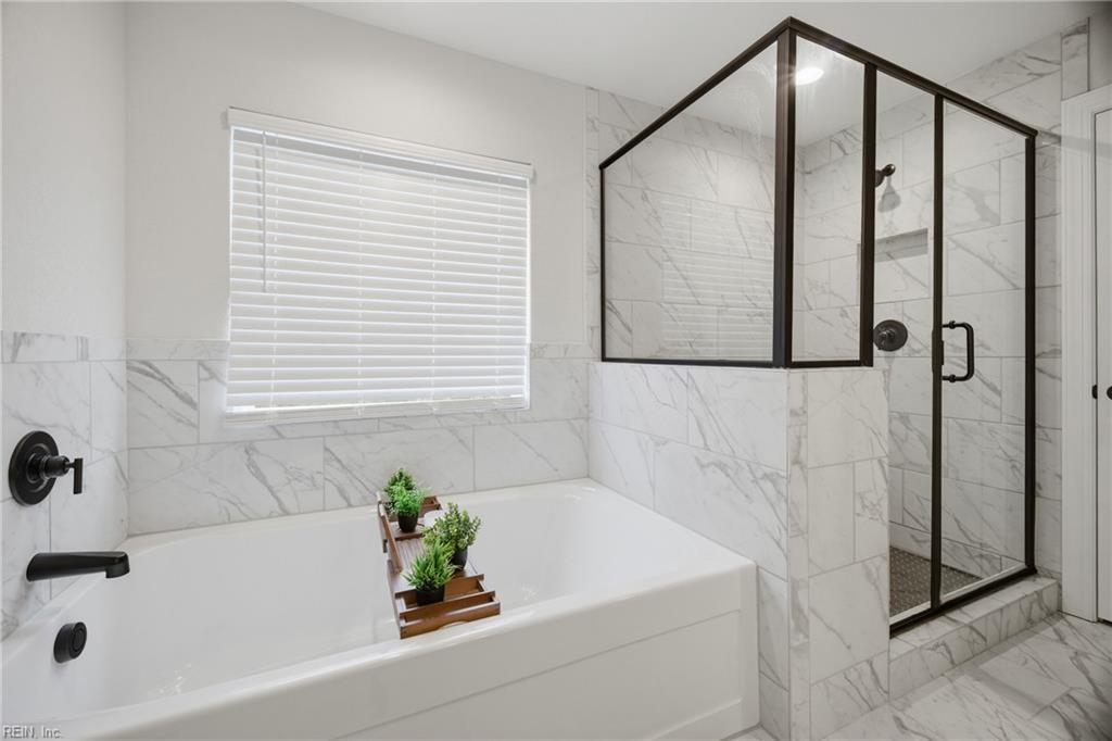 Bathroom with a white soaking tub, marble-look tile, and black-framed glass shower.