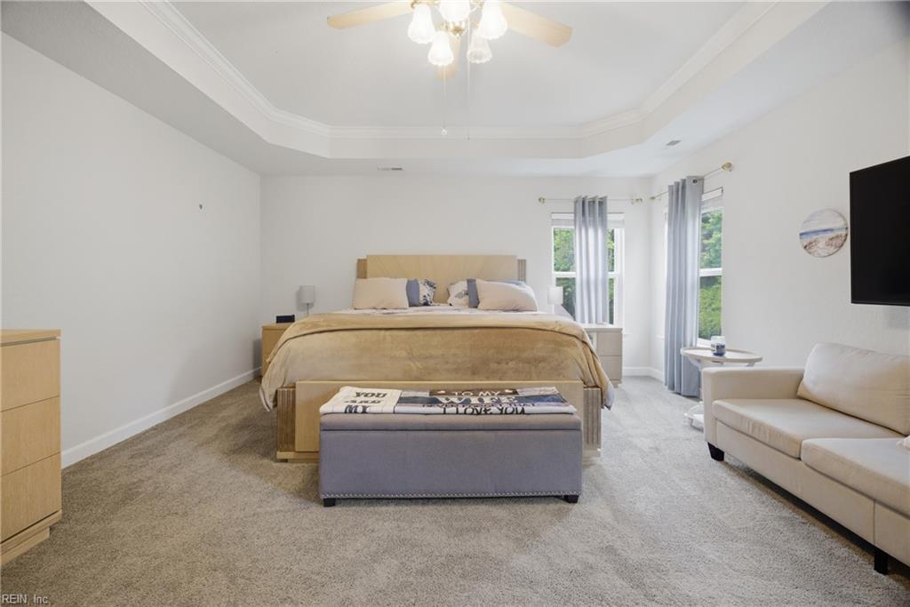 Spacious bedroom with a central bed, tray ceiling, bay windows, and a white sofa.