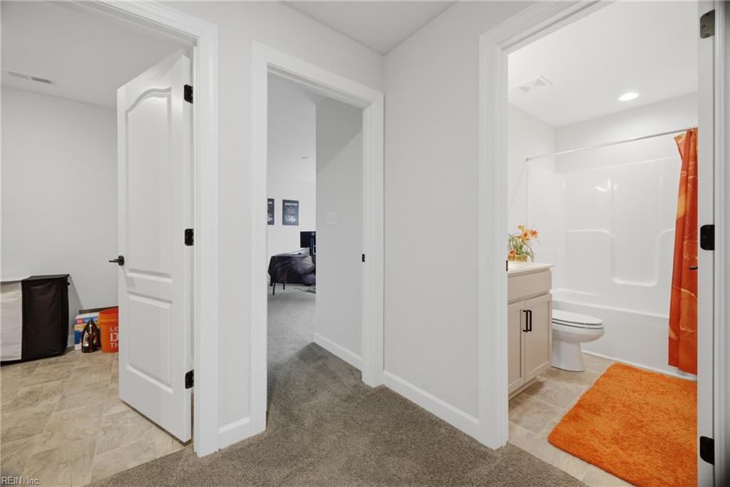 Hallway opening to a bathroom with a white tub and shower and bright orange accents.