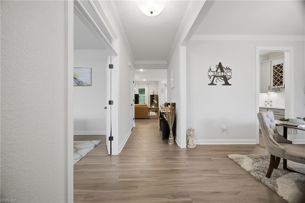 Wide hallway with light wood-look floors, opening to a living area and adjacent dining space.