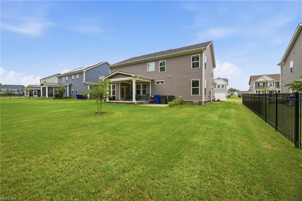 Rear of a two-story home with a covered patio, broad lawn, and black metal fence.