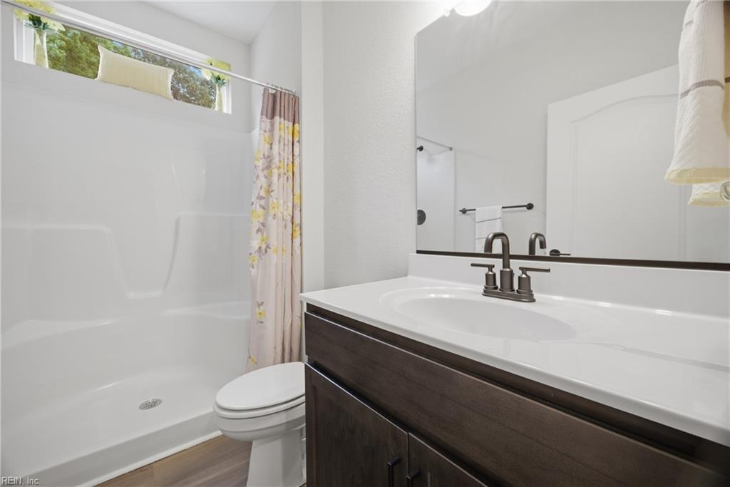 Bathroom with a white tub, floral shower curtain, toilet, and dark wood vanity.