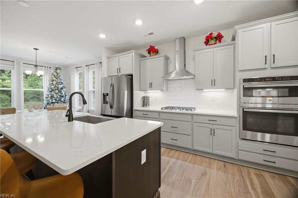 Bright kitchen with a large white-topped island, stainless steel appliances, and a Christmas tree by the windows.