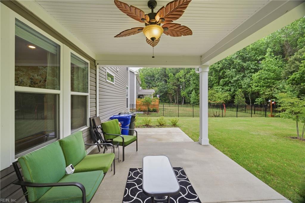Covered patio with green seating, a ceiling fan, and a fenced, tree-lined backyard.