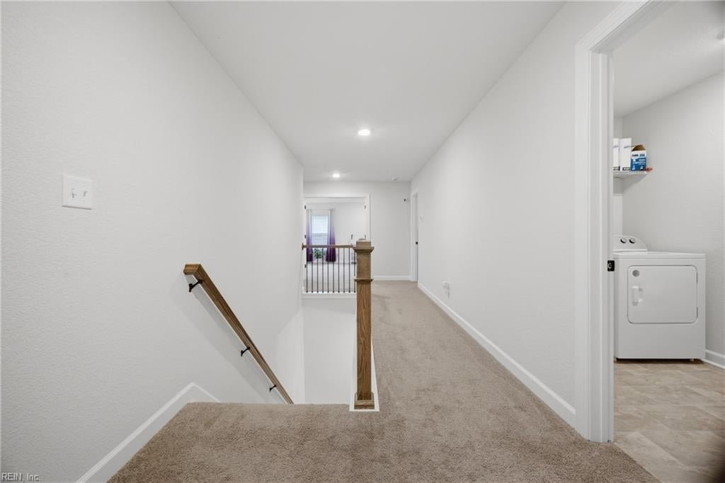 Carpeted upstairs landing with a wooden stair railing and doorway to a laundry room.
