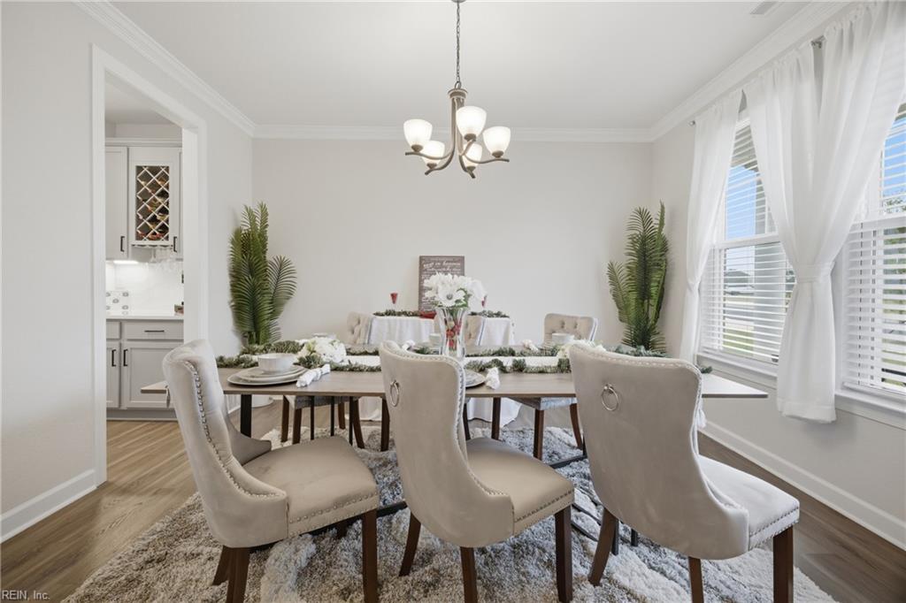 Staged dining room with a set table, upholstered chairs, chandelier, and tall curtained windows.