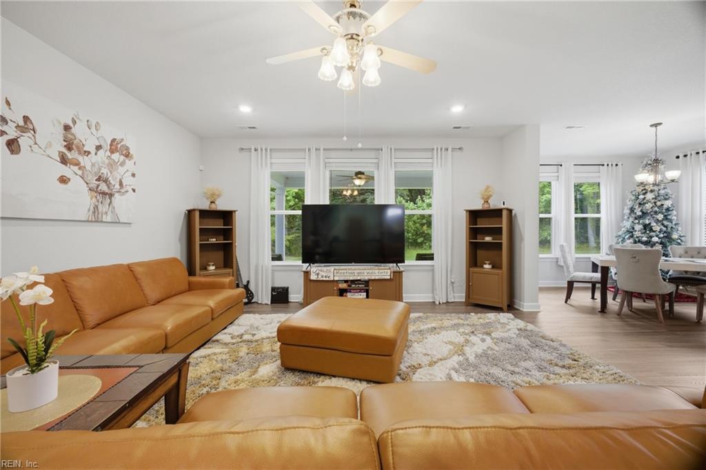 Living room with tan leather seating, television, large windows, and adjoining dining area.
