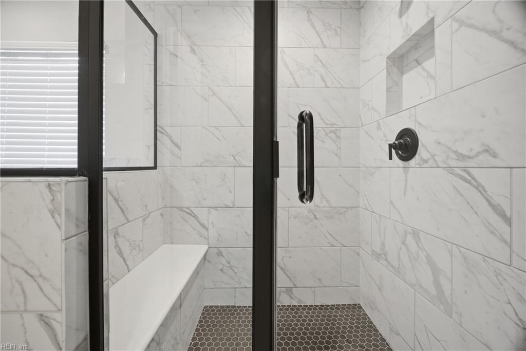 Walk-in shower with marble-look tile, a built-in bench, and black-framed glass door.