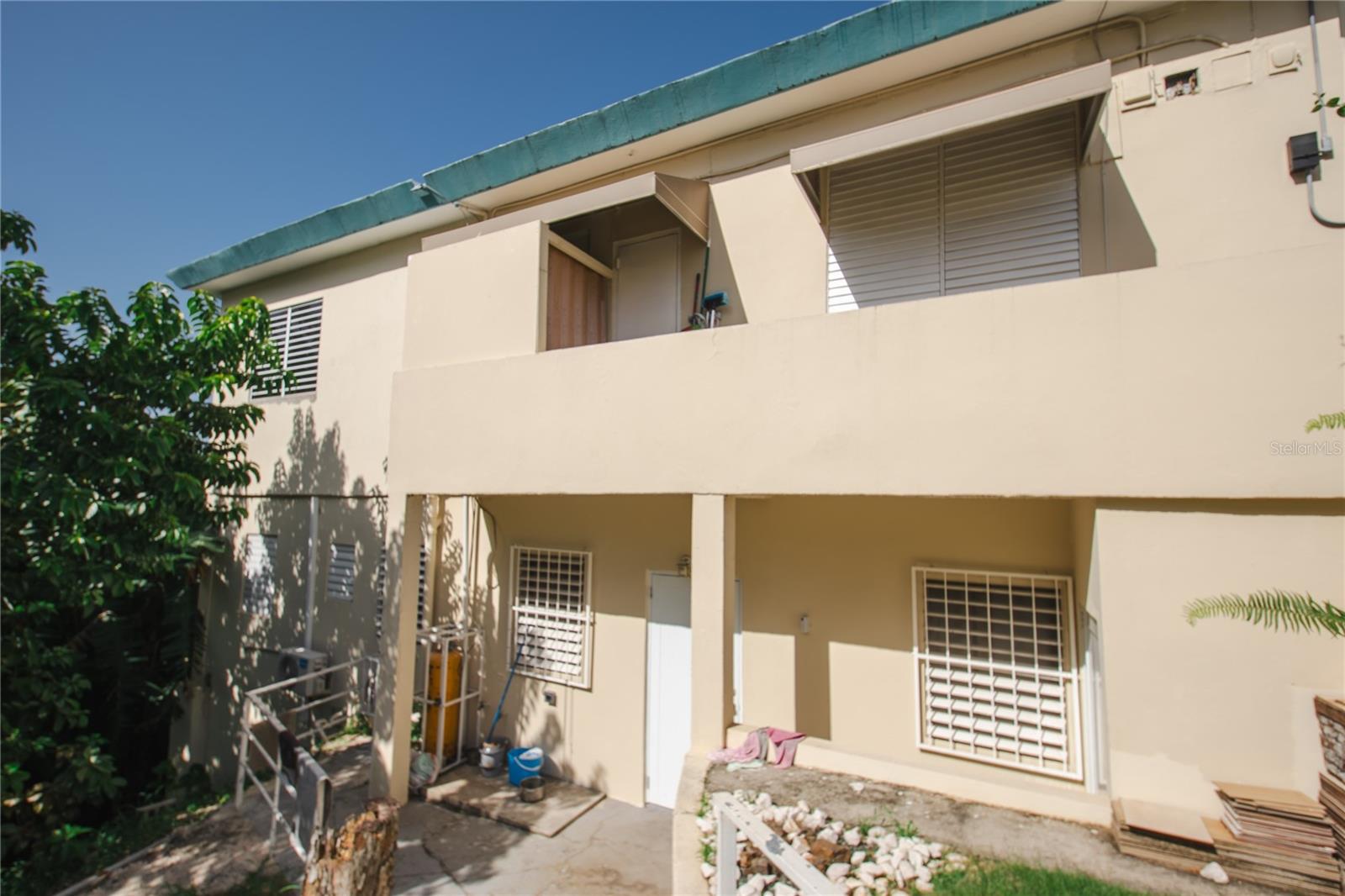 Beige two-story residential building with teal roof trim, barred windows, and a shaded entry walkway.