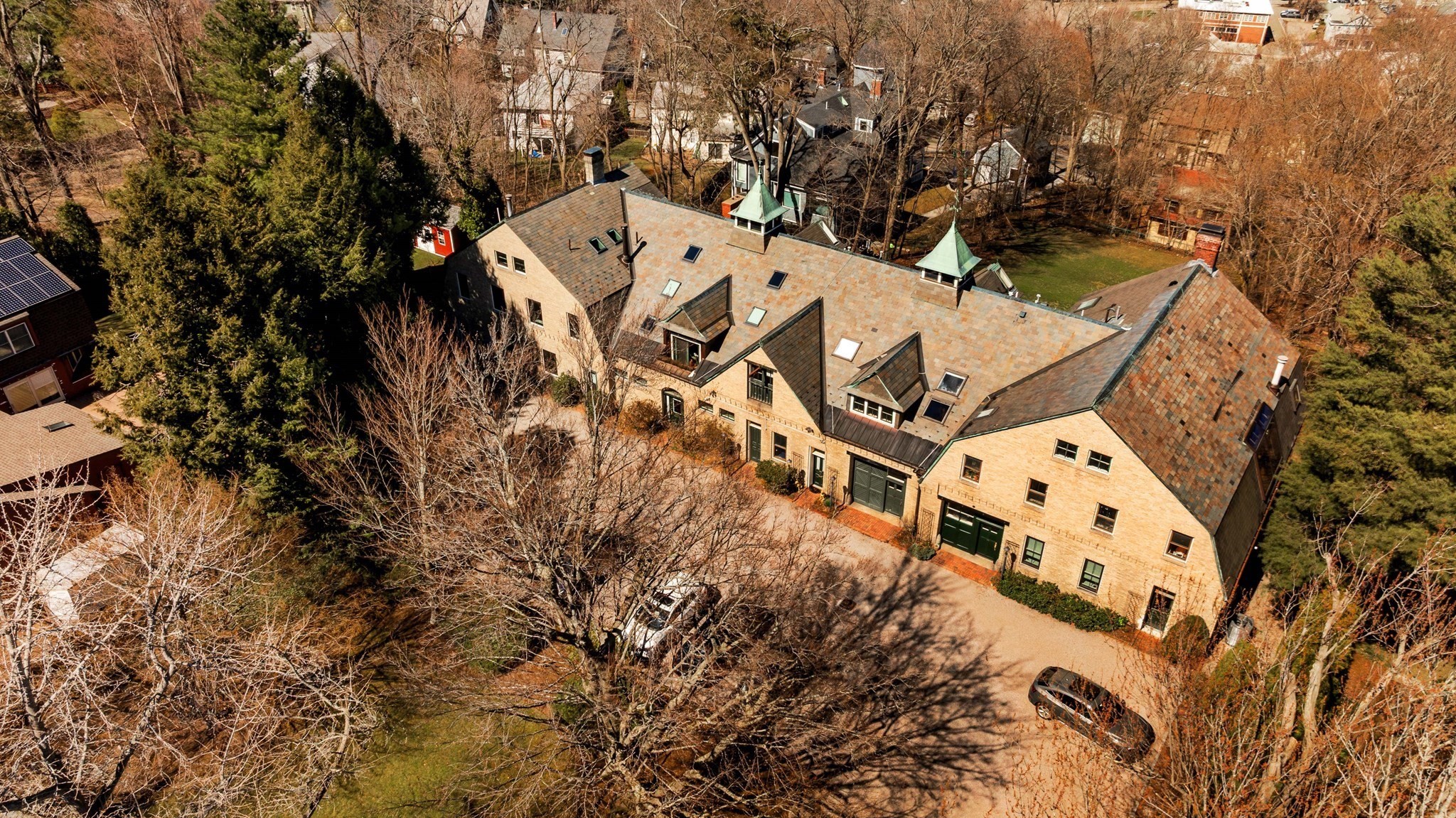 Aerial view of a stone building with slate roofs and green-topped turrets among leafless trees.