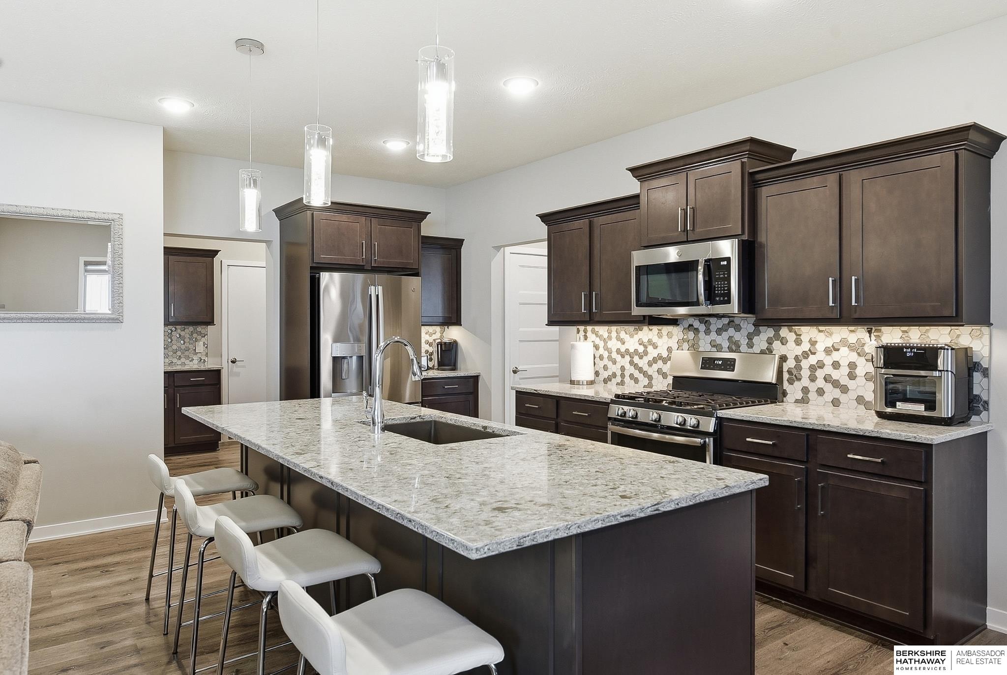 Kitchen with dark cabinets, hexagonal backsplash, stainless appliances, and a large island.