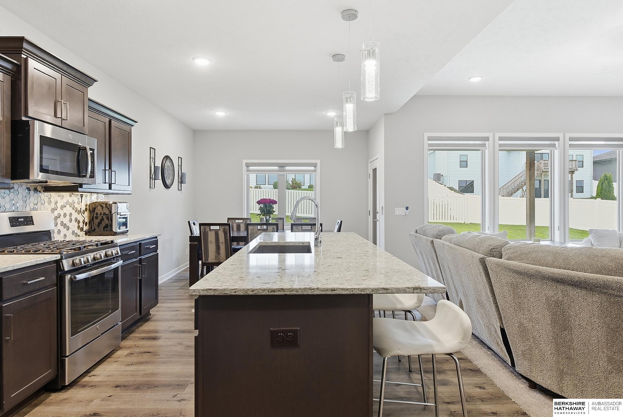 Open-plan kitchen with a large granite island, dark cabinetry and stainless steel appliances beside the living area.