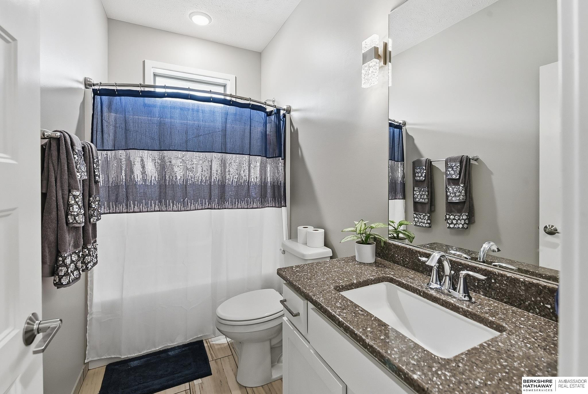 Bathroom with a dark speckled vanity countertop, large mirror, and blue-and-gray shower curtain.