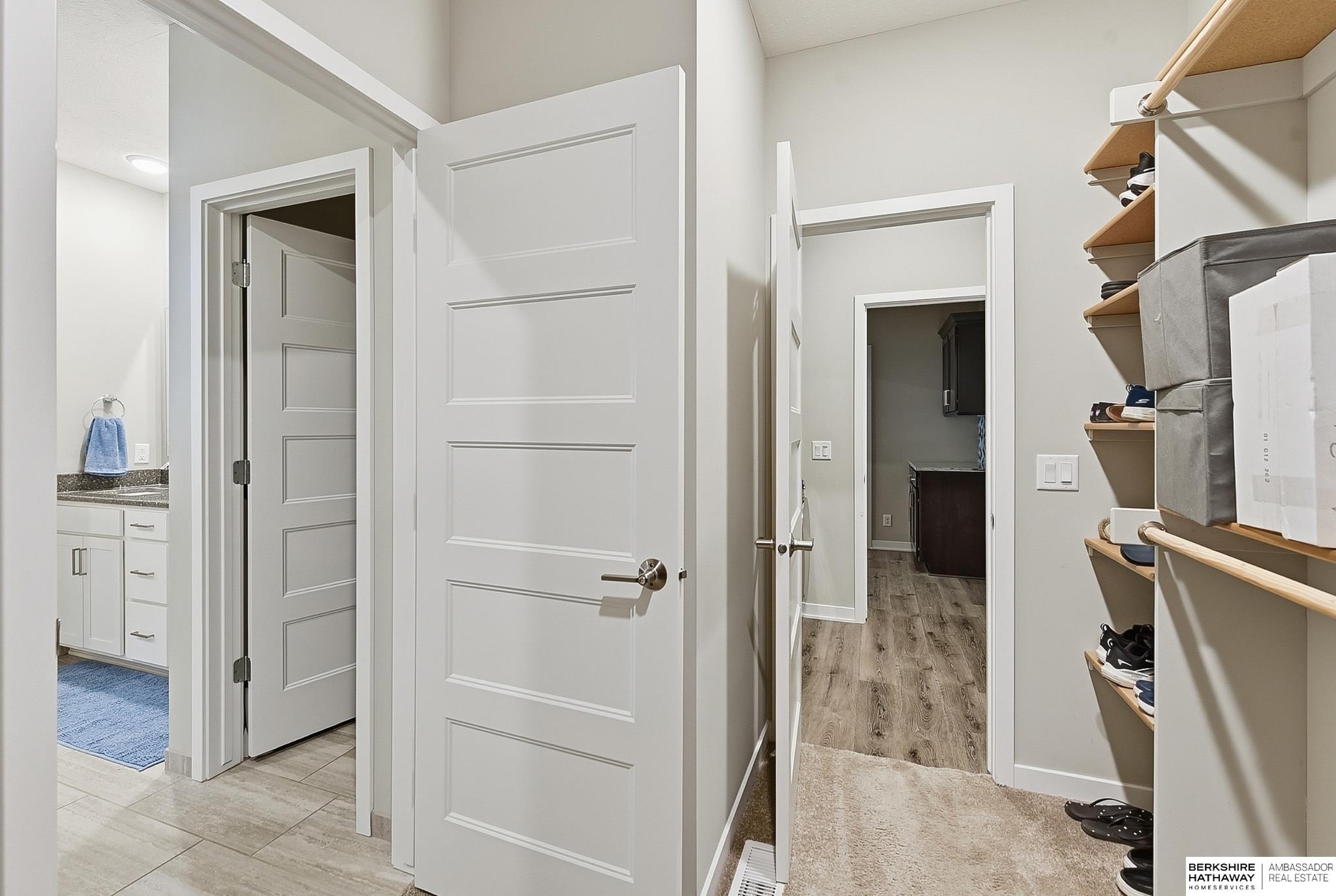 Walk-in closet with open shoe shelves, storage bins, and doors to a bathroom and hallway.