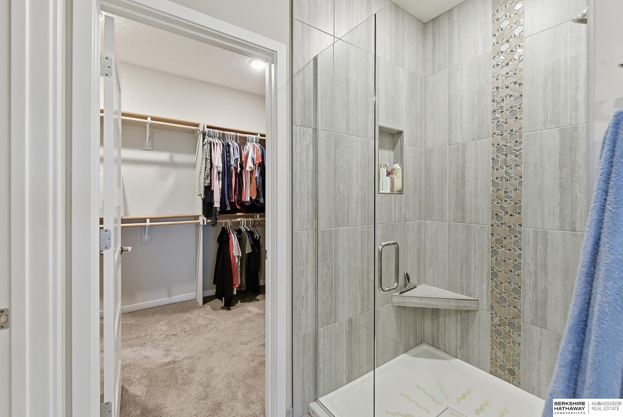 Walk-in shower beside a carpeted closet with hanging clothes and a glass shower enclosure.