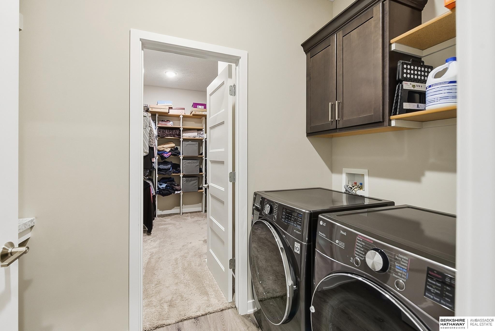 Laundry room with dark washer and dryer, wall cabinets, and an open doorway to a walk-in closet.