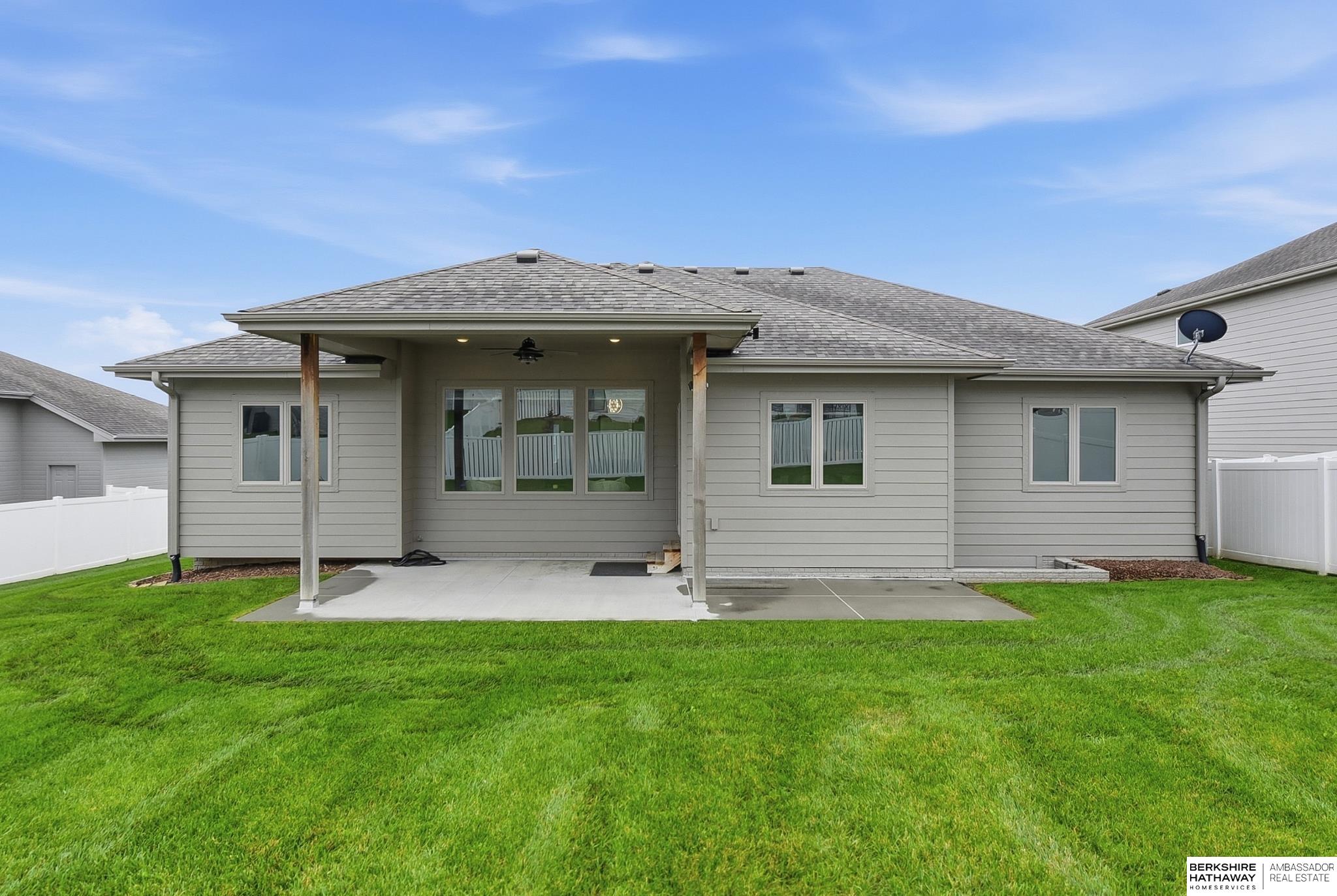 Rear of a gray-sided home with a covered patio, broad lawn, and white fenced yard.