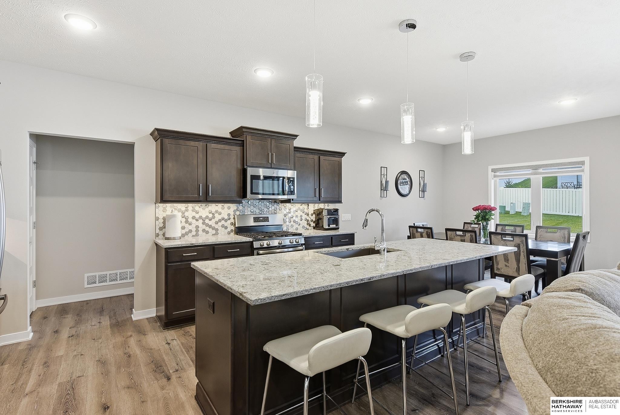 Open kitchen and dining area with a large granite island, dark cabinets, and stainless steel appliances.