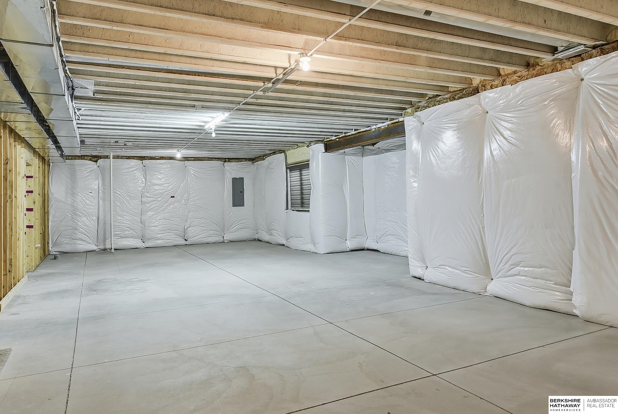 Unfinished basement with a concrete floor, exposed ceiling joists, and white wall insulation.