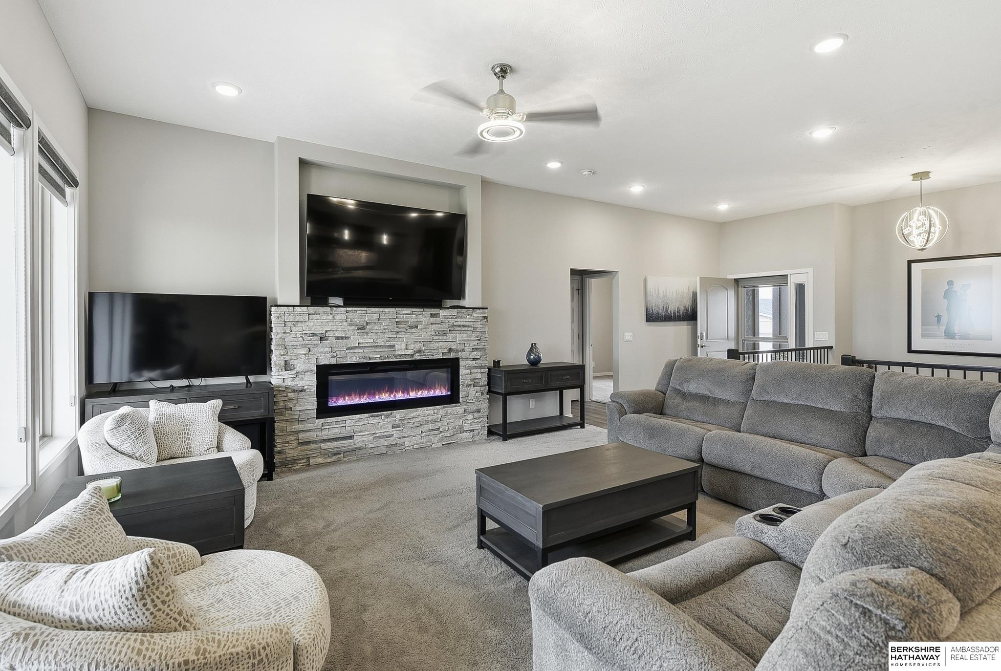 Living room with gray sectional sofas and a stone fireplace beneath a mounted television.