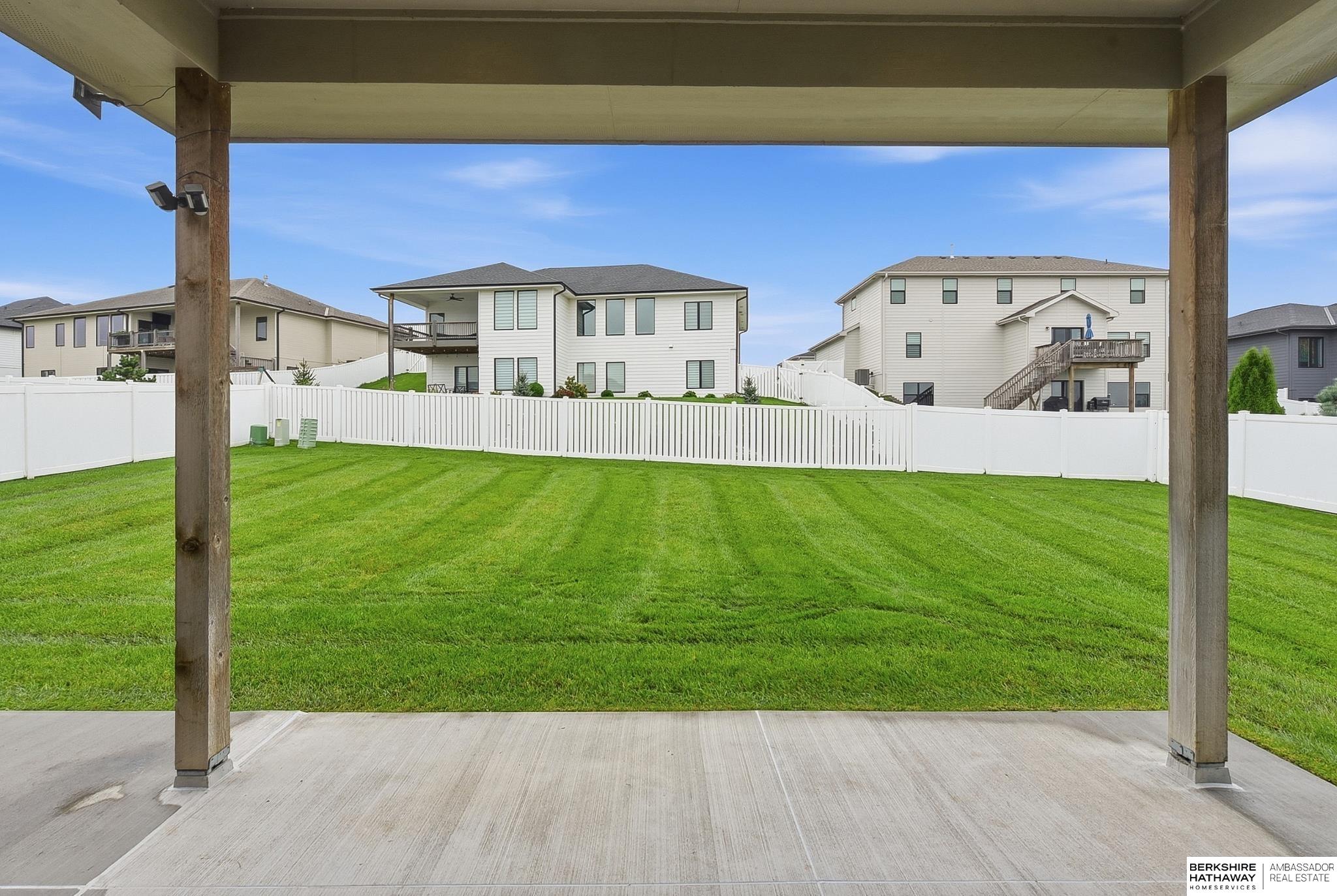 Fenced backyard with a broad green lawn, viewed from beneath a covered patio.