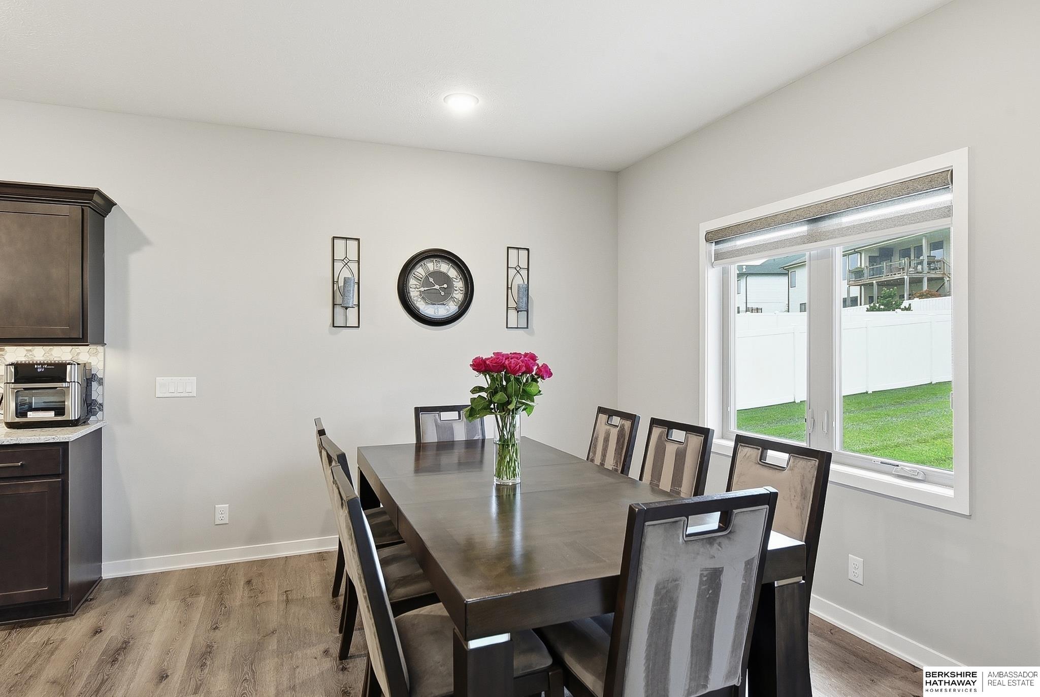 Dining room with a dark wood table, pink roses, and a large window overlooking the fenced lawn.