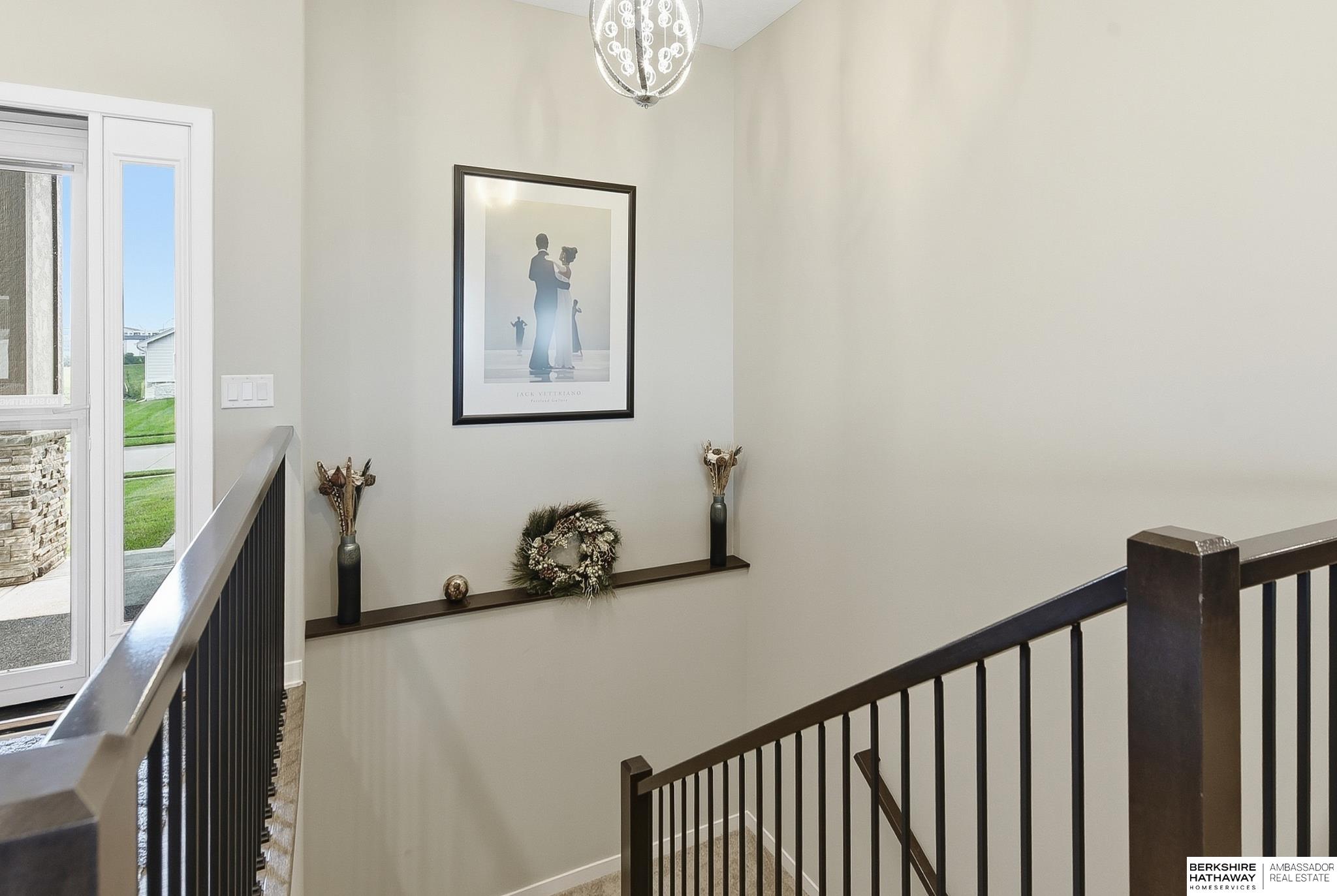 Stairwell with dark railings, framed artwork, and a decorative shelf.