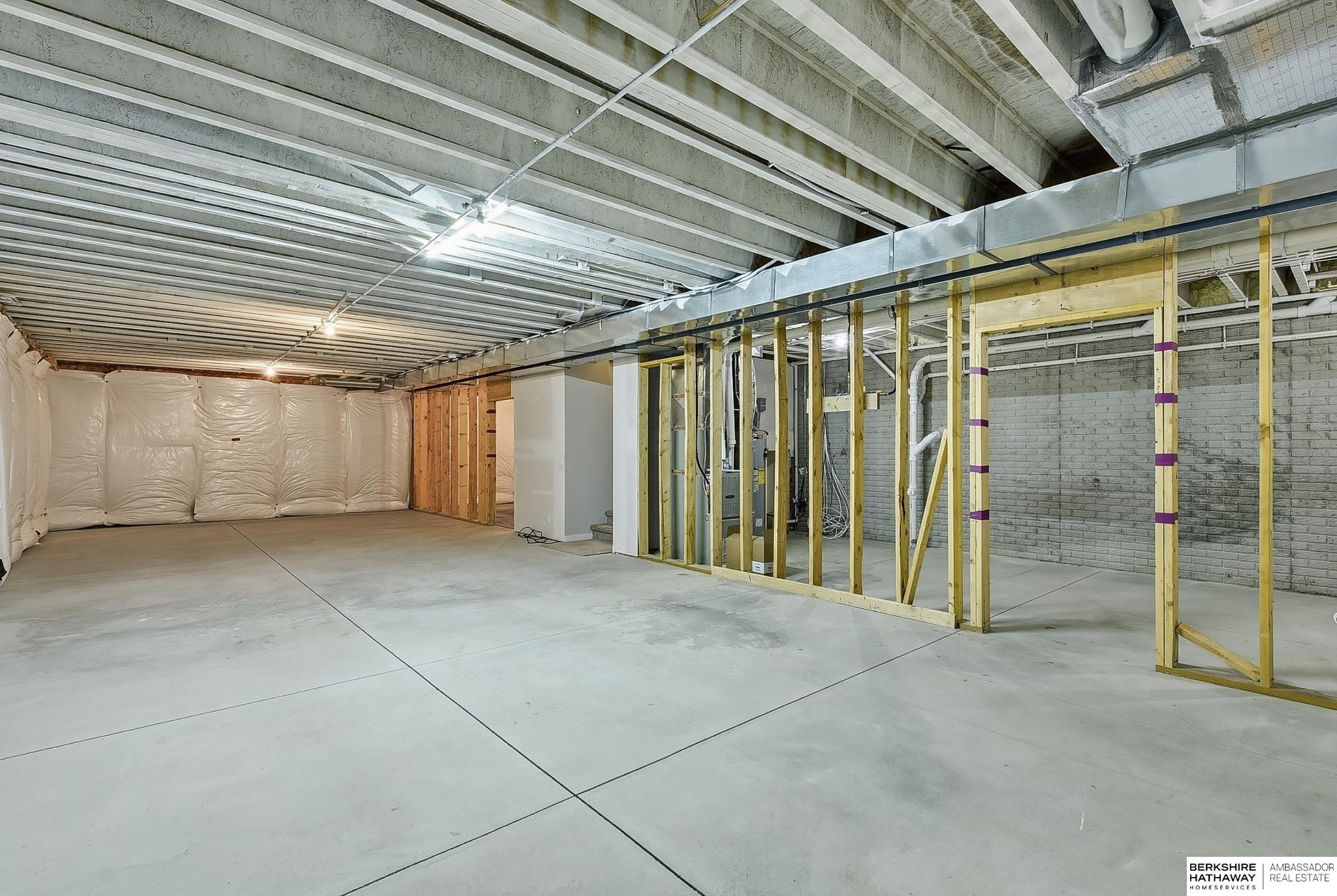 Unfinished basement with exposed framing, ceiling joists, ductwork, and a broad concrete floor.