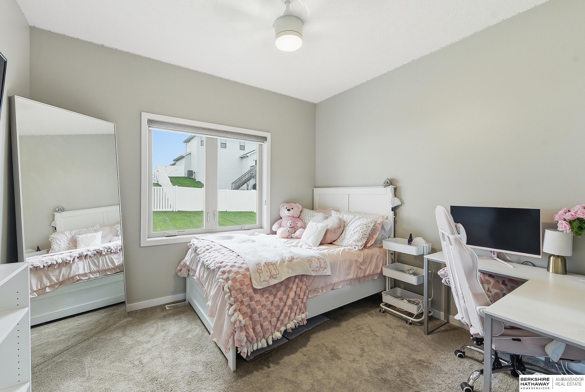 Furnished bedroom with pink bedding, a full-length mirror, and a desk beside the window.