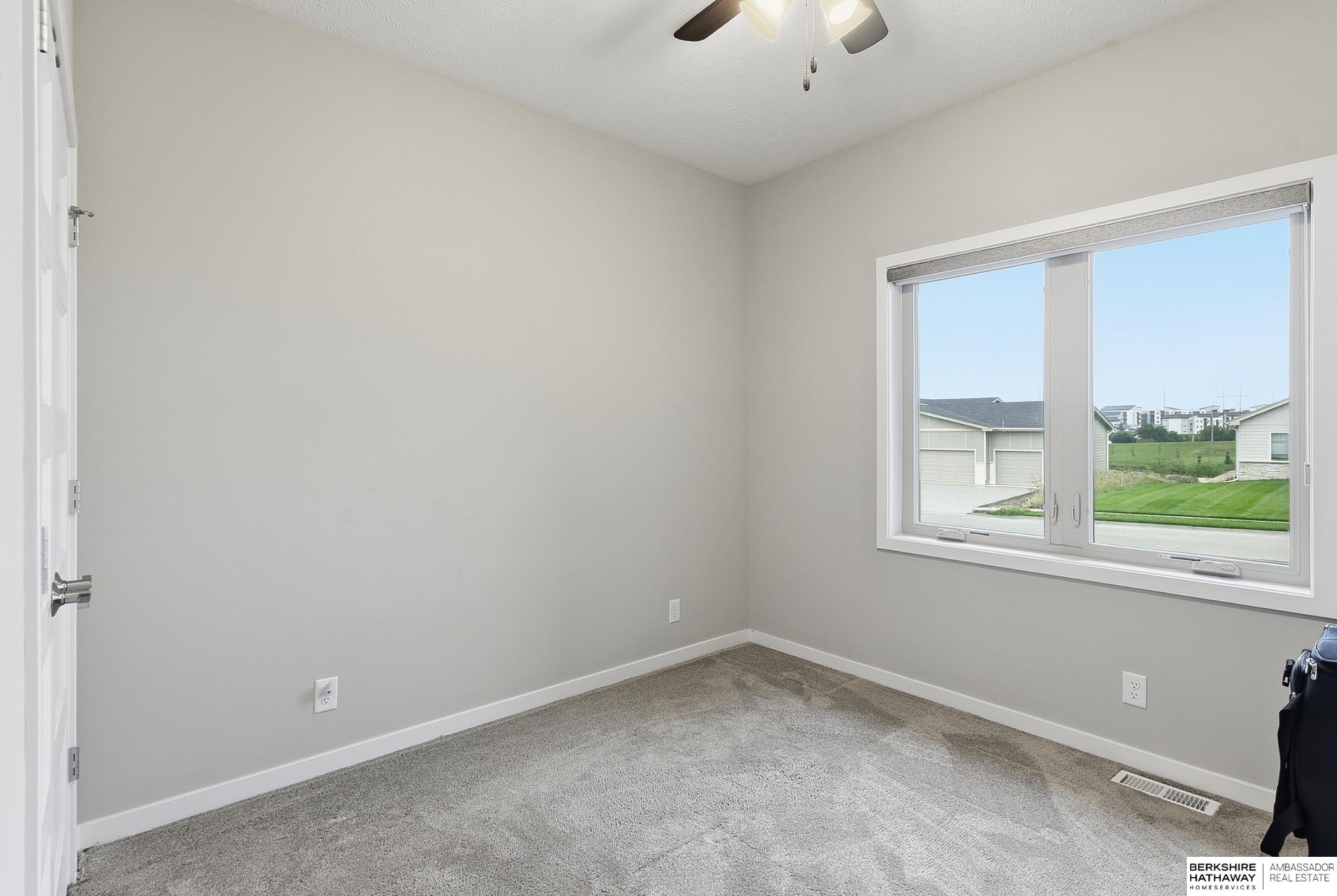 Empty carpeted bedroom with a wide window overlooking neighboring homes and a lawn.