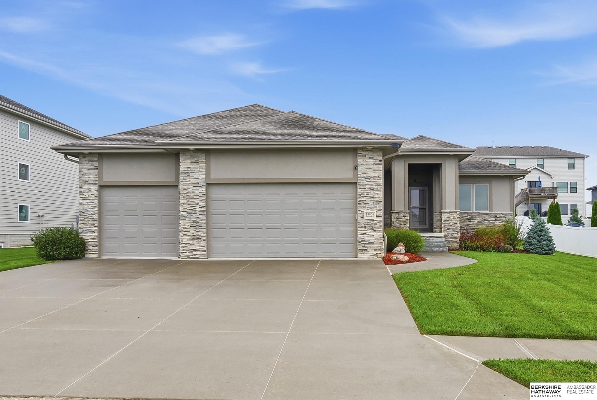 Single-story home with stone accents, a broad two-car garage, landscaped entry, and concrete driveway.
