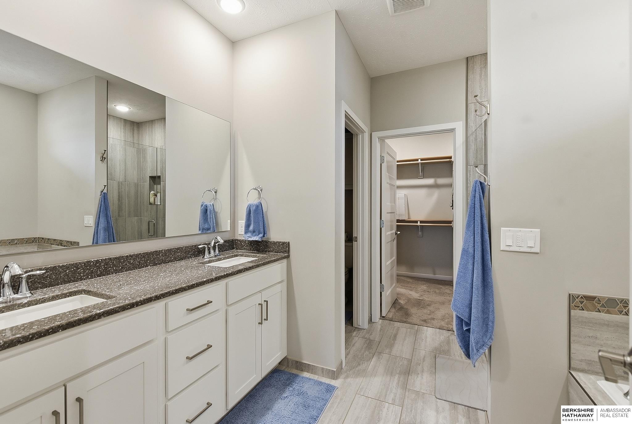 Bathroom with a white double vanity, speckled countertop, large mirror, and open closet.